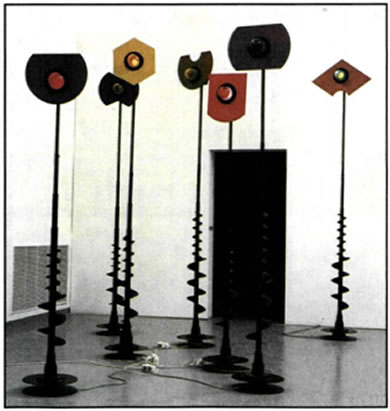 Τάκης (Βασιλάκης) (γενν. το 1925), «Φωτεινά σινιάλα», 1985, ύψος 2,5-3 μ., Ιδιωτική Συλλογή, Παρίσι. Στον χώρο της κινητικής τέχνης ο Τάκης δημιούργησε τους δικούς του εκφραστικούς τρόπους, αξιοποιώντας φυσικές δυνάμεις, όπως ο ηλεκτρομαγνητισμός, το φως και ο ήχος. Η σειρά «Σινιάλα» είναι κινητικά γλυπτά, τα οποία αποτελούνται από αυτοφωτιζόμενες κατασκευές αλουμινίου, στηριγμένες σε εύκαμπτες Βέργες που ταλαντεύονται συνεχώς, δημιουργώντας σχέση αλληλεπίδρασης τόσο μεταξύ τους όσο και με το περιβάλλον και δίνοντας ένα αποτέλεσμα δύναμης, αλλά και ποιητικής ευαισθησίας.